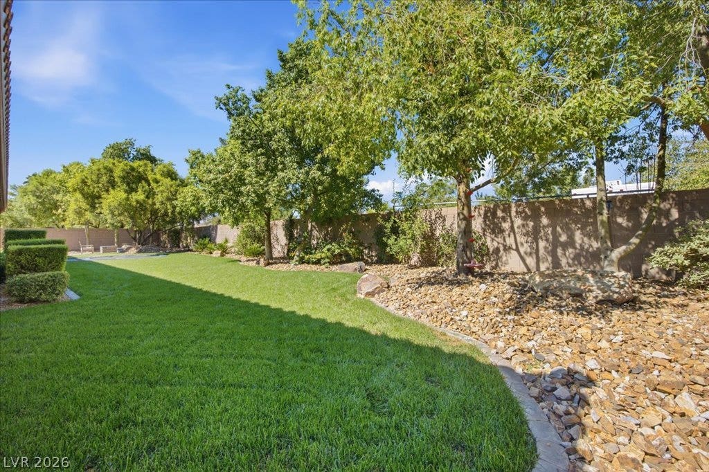8030 Palm Cove Court, Las Vegas, NV 89129 Mature trees line a stone-bordered lawn bordering the perimeter wall.
