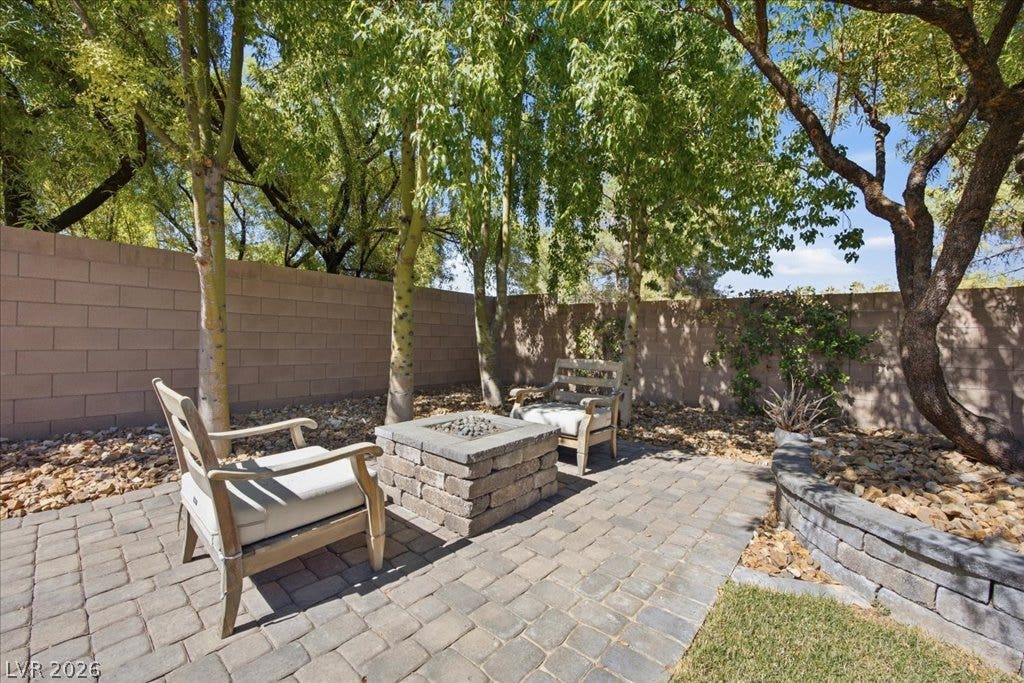 8030 Palm Cove Court, Las Vegas, NV 89129 Mature trees shade a paved patio featuring a built-in stone fire pit and privacy wall.