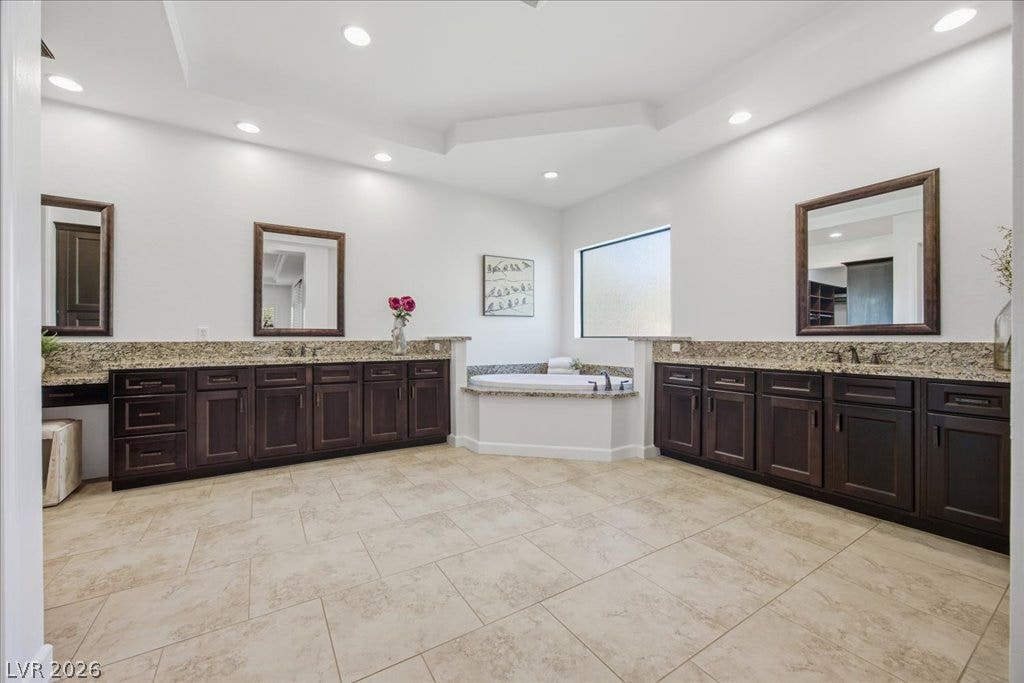 8030 Palm Cove Court, Las Vegas, NV 89129 Double vanities with stone counters flank a central soaking tub under recessed lighting.