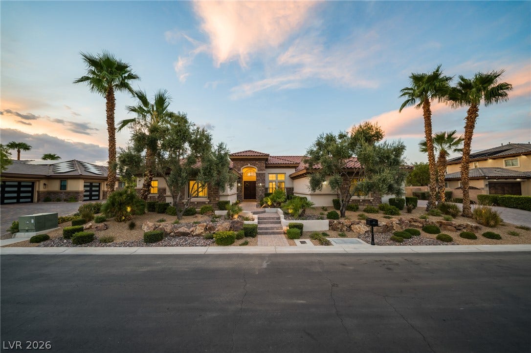 8030 Palm Cove Court, Las Vegas, NV 89129 Manicured desert landscaping and towering palms frame a grand stone-accented facade under dramatic twilight skies.