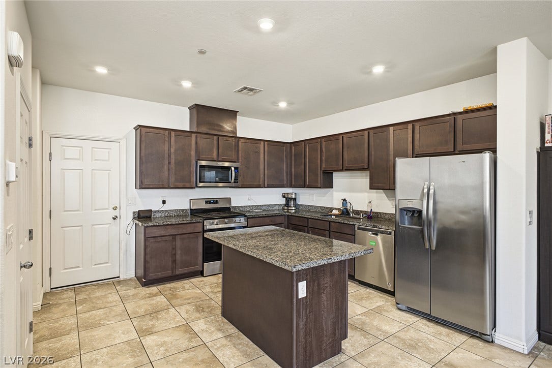 1180 Gypsum Hills Court, Henderson, NV 89002 Gleaming tile floors anchor dark cabinetry and a central island with granite countertops.
