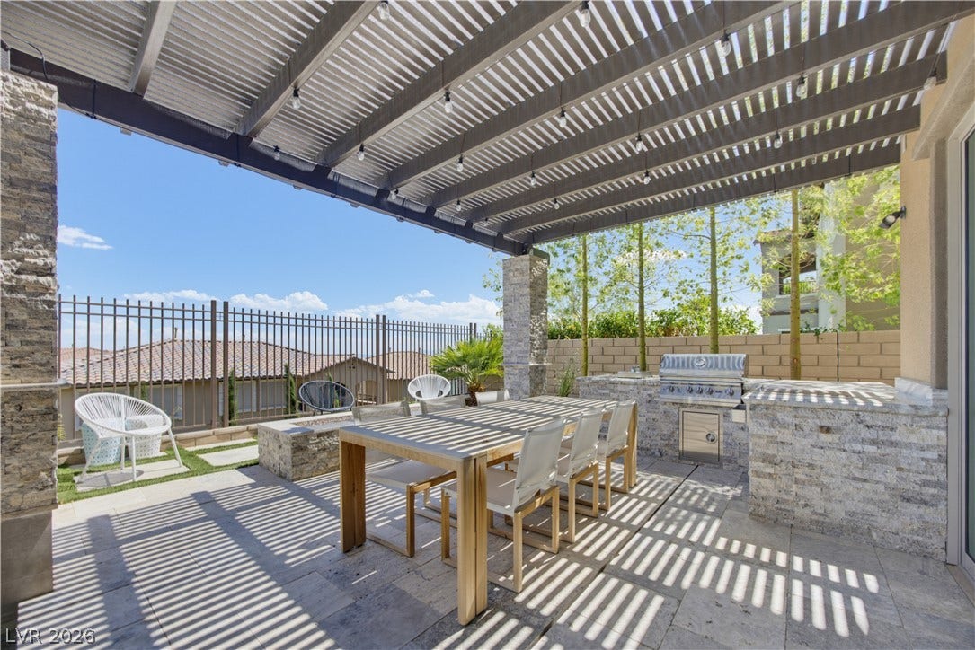 446 Bosco Di Fiore Street, Las Vegas, NV 89138 A spacious stone-tiled patio lies beneath a modern metal pergola with a built-in outdoor kitchen.