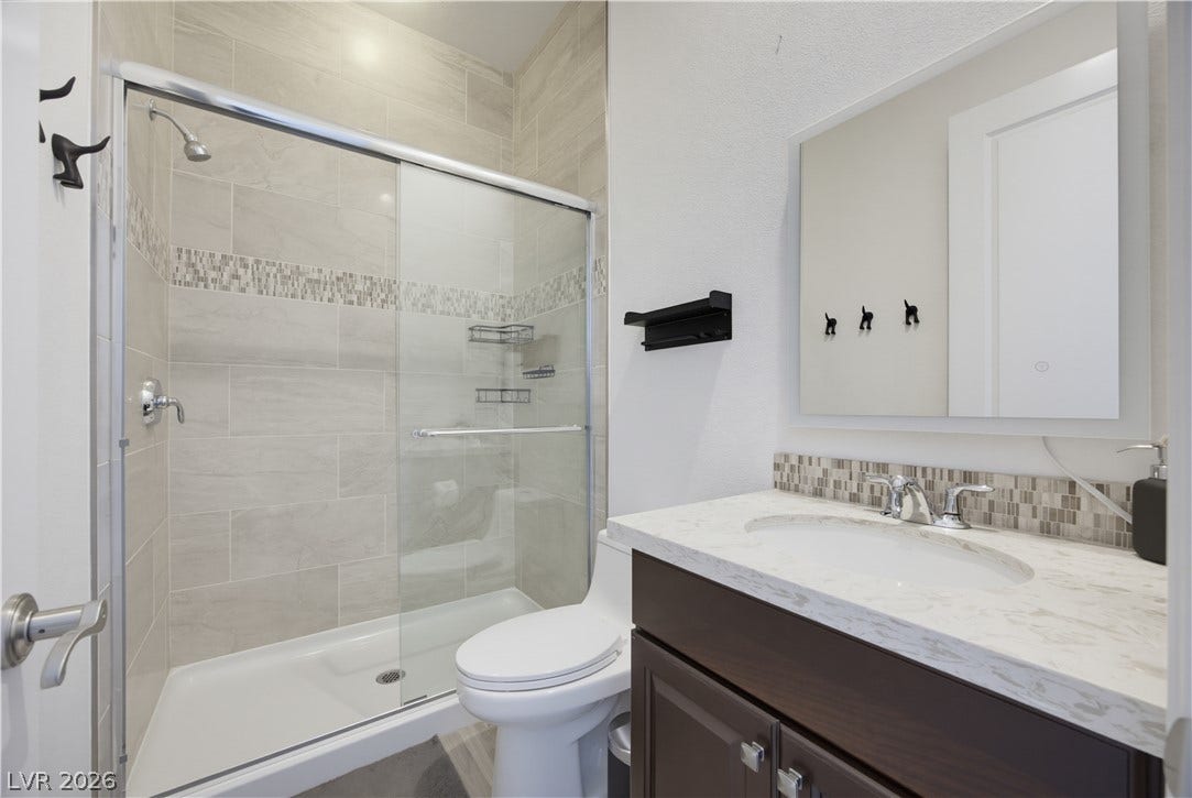 446 Bosco Di Fiore Street, Las Vegas, NV 89138 A modern bathroom features a glass-enclosed shower, stone counters, and elegant tiled accents.