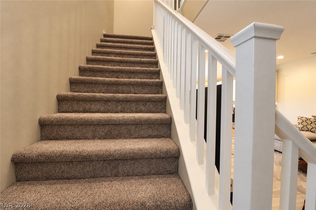 Carpeted stairs ascend alongside a classic white banister under high ceilings.