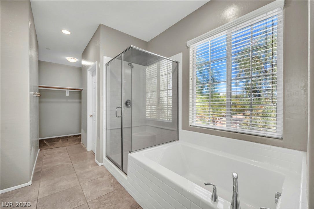 8577 Insignia Avenue, #101, Las Vegas, NV 89178 A glass-enclosed shower stands alongside a tiled soaking tub under a large window.