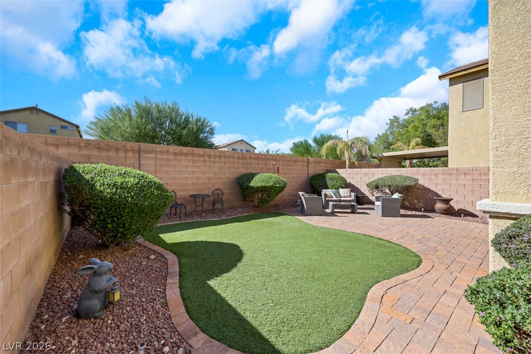 An inviting backyard features a manicured lawn bordered by handsome paver stone patios.