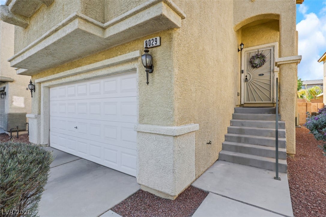 Stucco exterior finishes and concrete stairs lead to a covered front entry next to the garage.