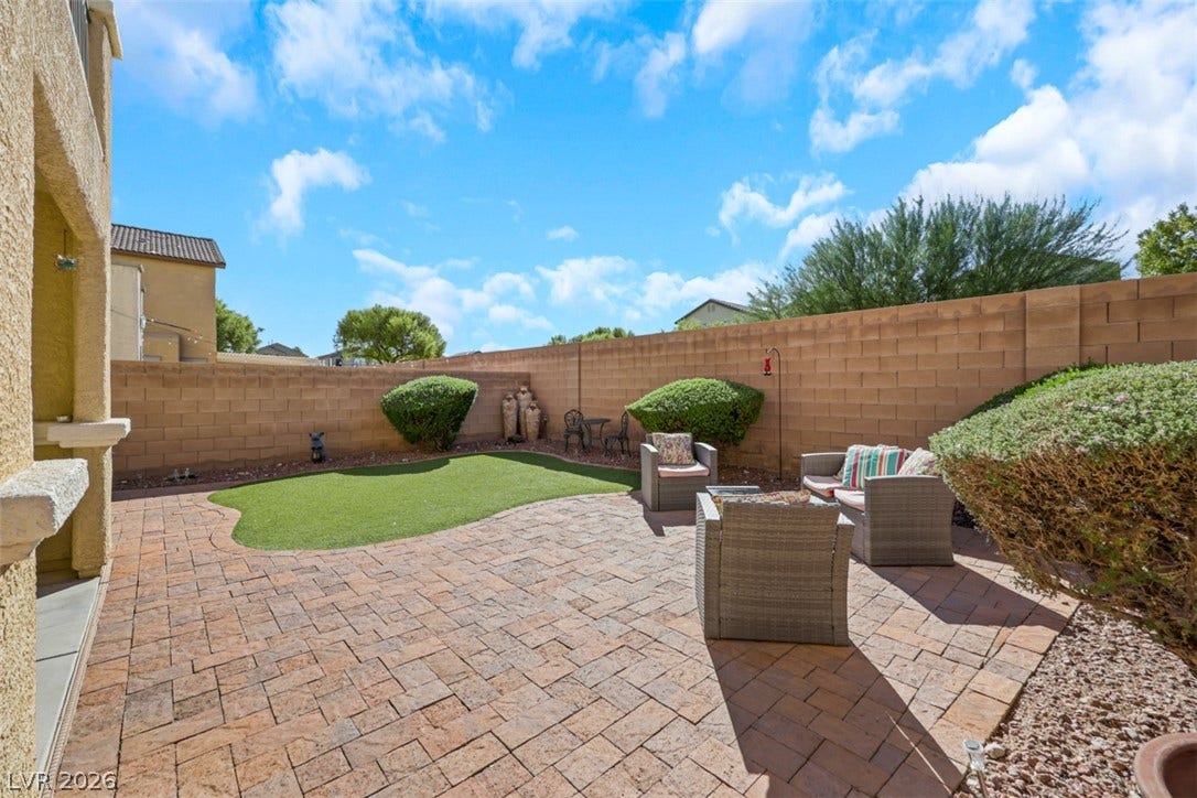 A spacious brick paver patio opens to a manicured lawn enclosed by block wall fencing.