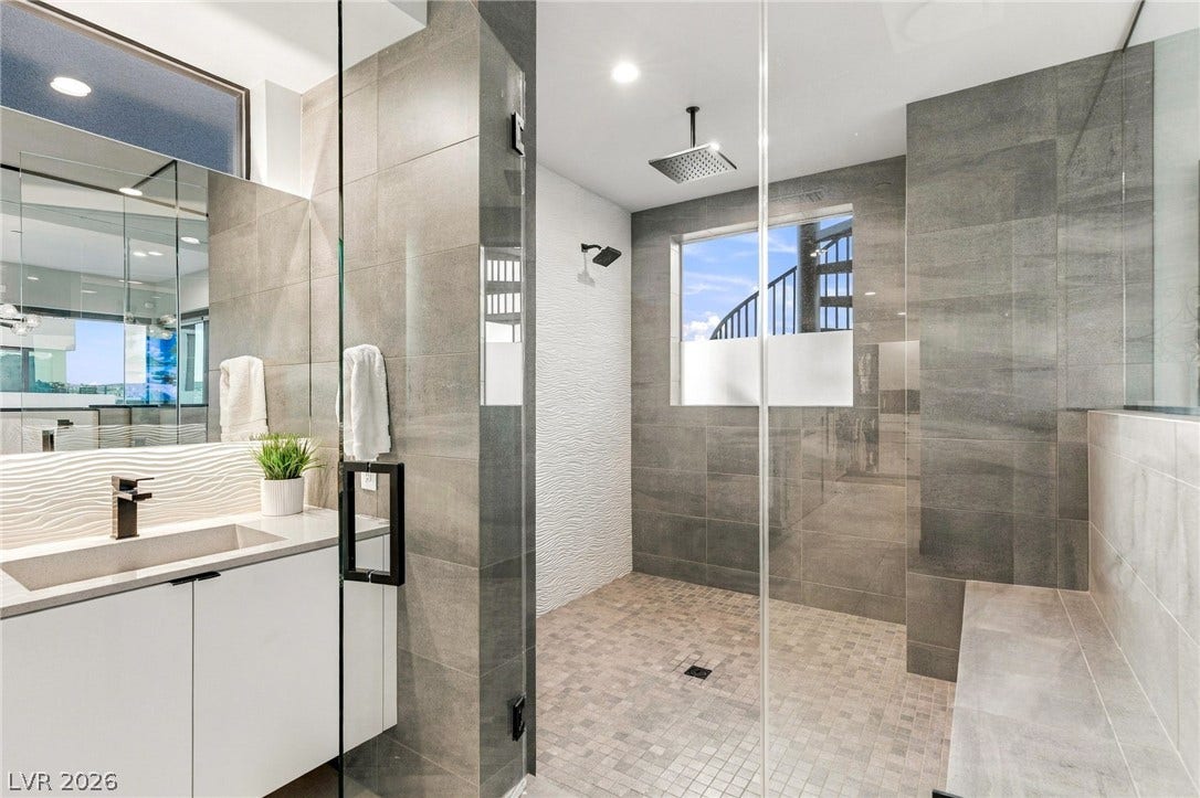 18 Heron Harbour Drive, Henderson, NV 89011 A glass-enclosed walk-in shower features modern tile and a built-in bench.