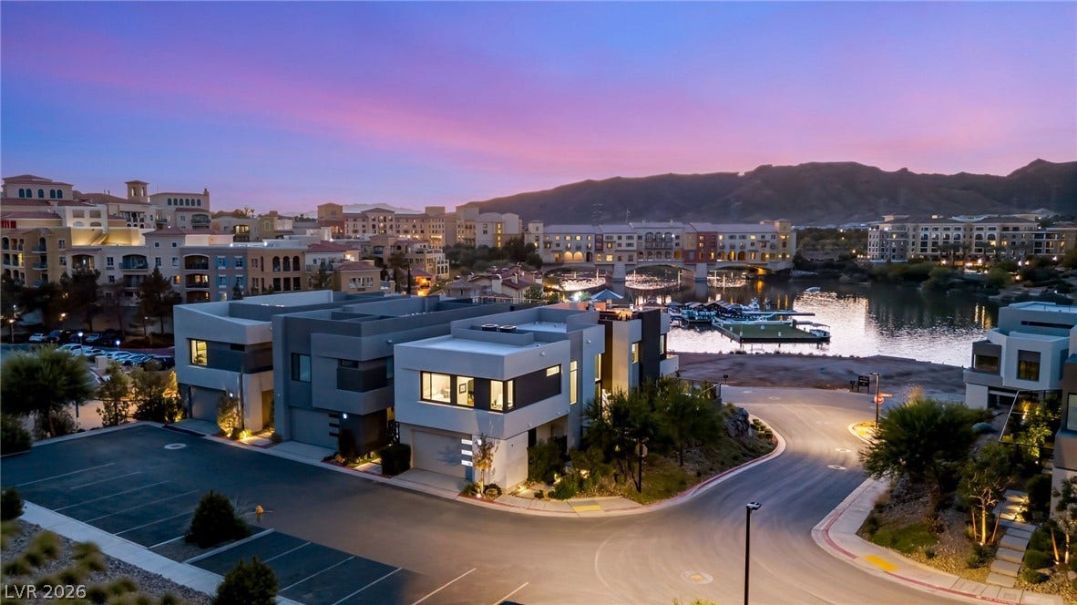 18 Heron Harbour Drive, Henderson, NV 89011 Modern lakeside residences stand against a backdrop of distant mountains at sunset.