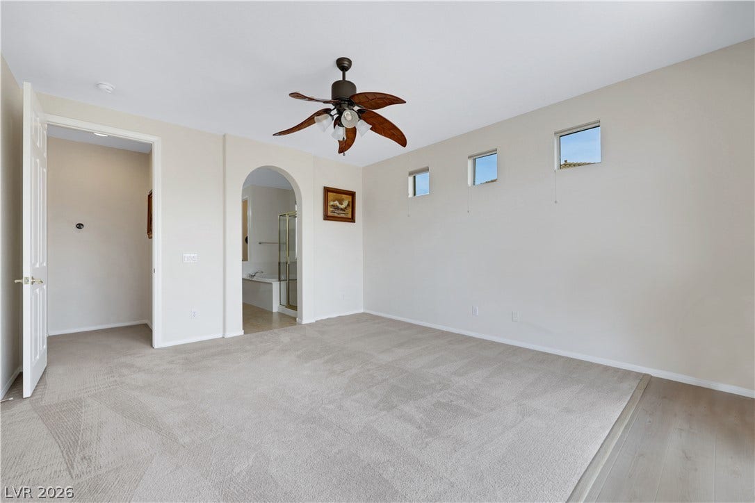 625 Bighorn Creek Street, Henderson, NV 89002 Well-lit primary bedroom featuring soft carpeting, a decorative ceiling fan, and arched entry to a private bathroom.