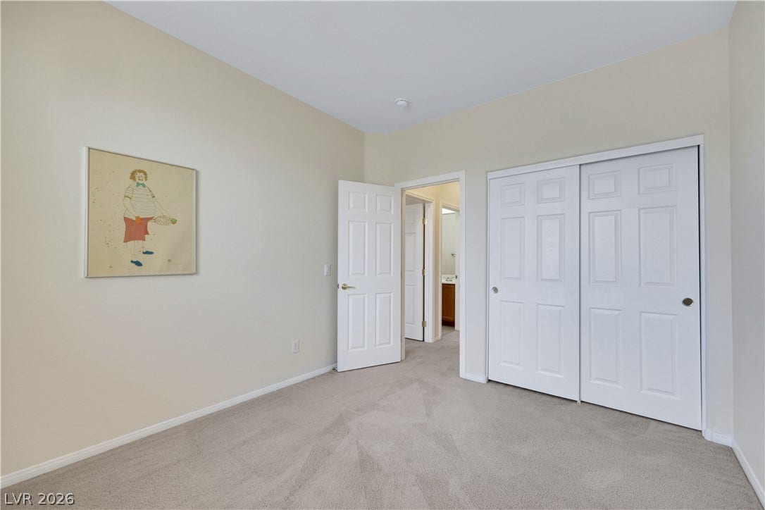 625 Bighorn Creek Street, Henderson, NV 89002 A well-proportioned bedroom features soft carpeting and ample closet space, with access to an adjacent bathroom.