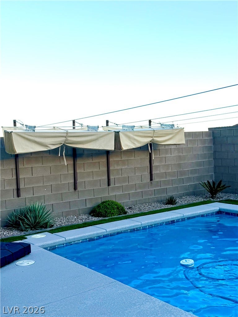 11725 Hatchling Avenue, Las Vegas, NV 89138 A sparkling blue pool sits alongside a clean masonry wall featuring retractable shade awnings.