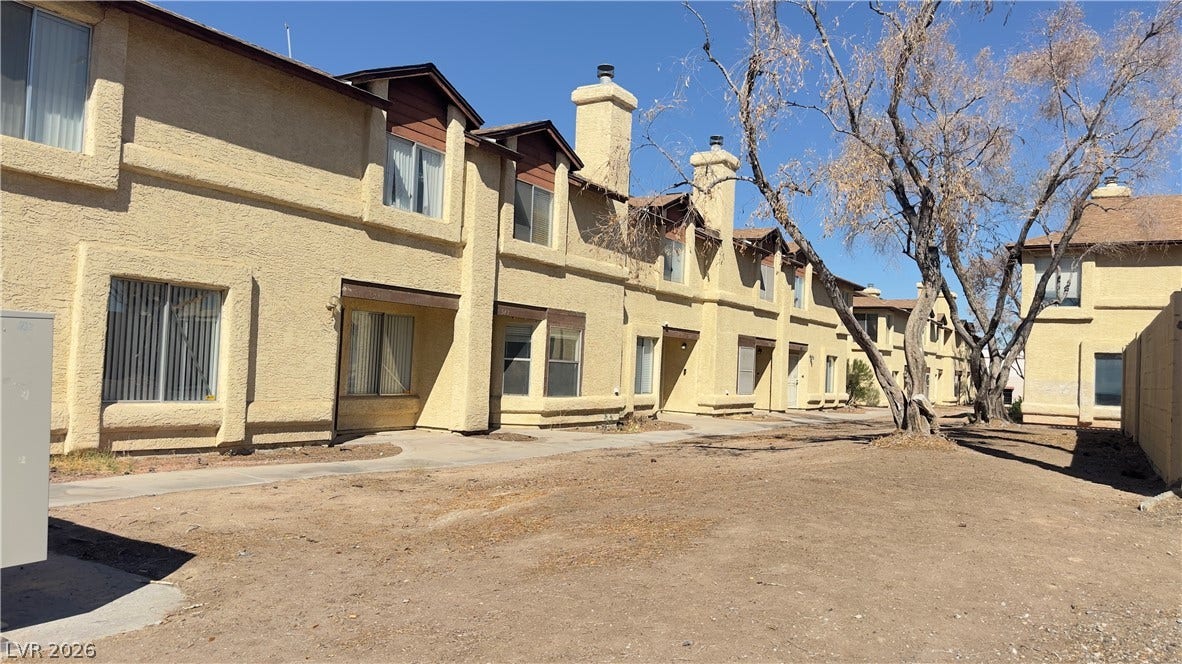 543 KRISTIN Lane, Henderson, NV 89011 Multi-level stucco townhomes stand under a clear blue sky alongside mature trees.