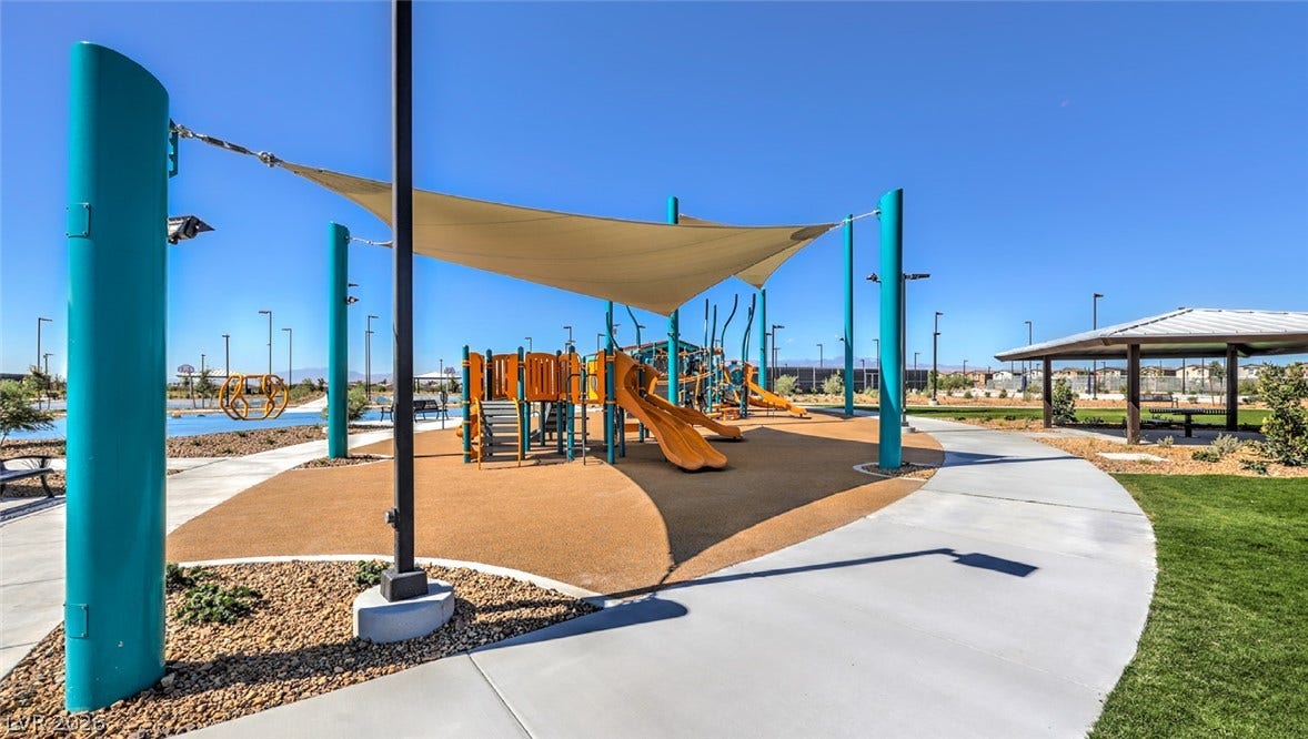 A vibrant community playground features slides and swings beneath a protective shade structure, complemented by a nearby covered picnic area.