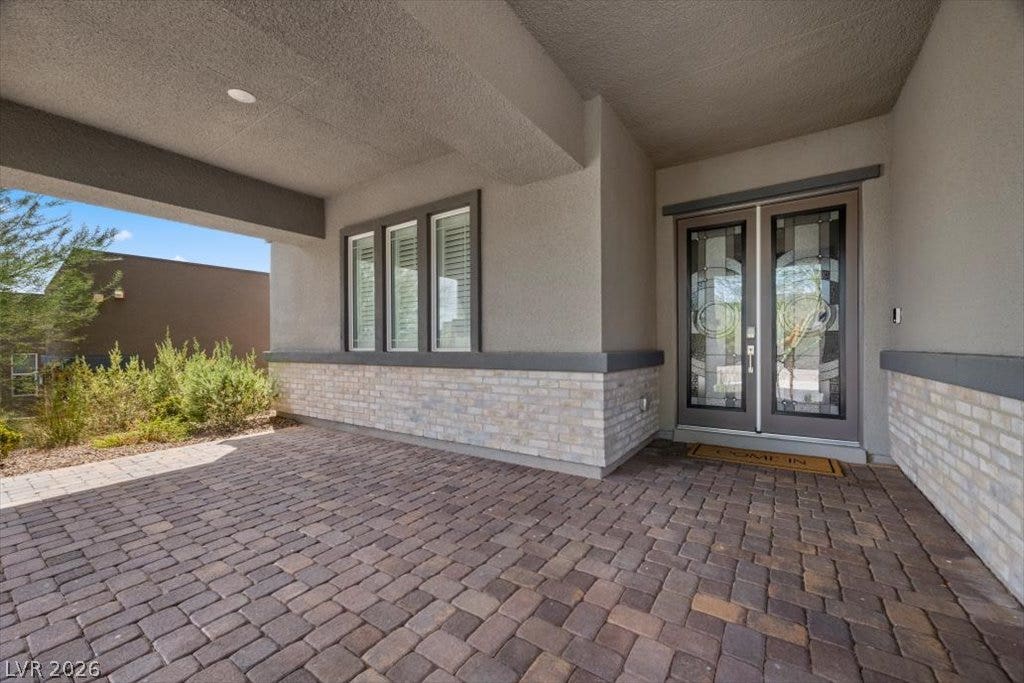 A sheltered entryway porch welcomes visitors with block pavers and stone wainscoting leading to decorative glass  double doors.