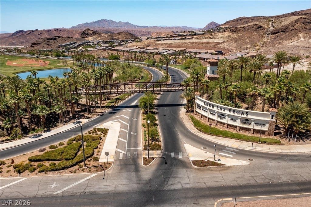 A grand gated community entrance frames the winding roadway under desert mountain peaks.