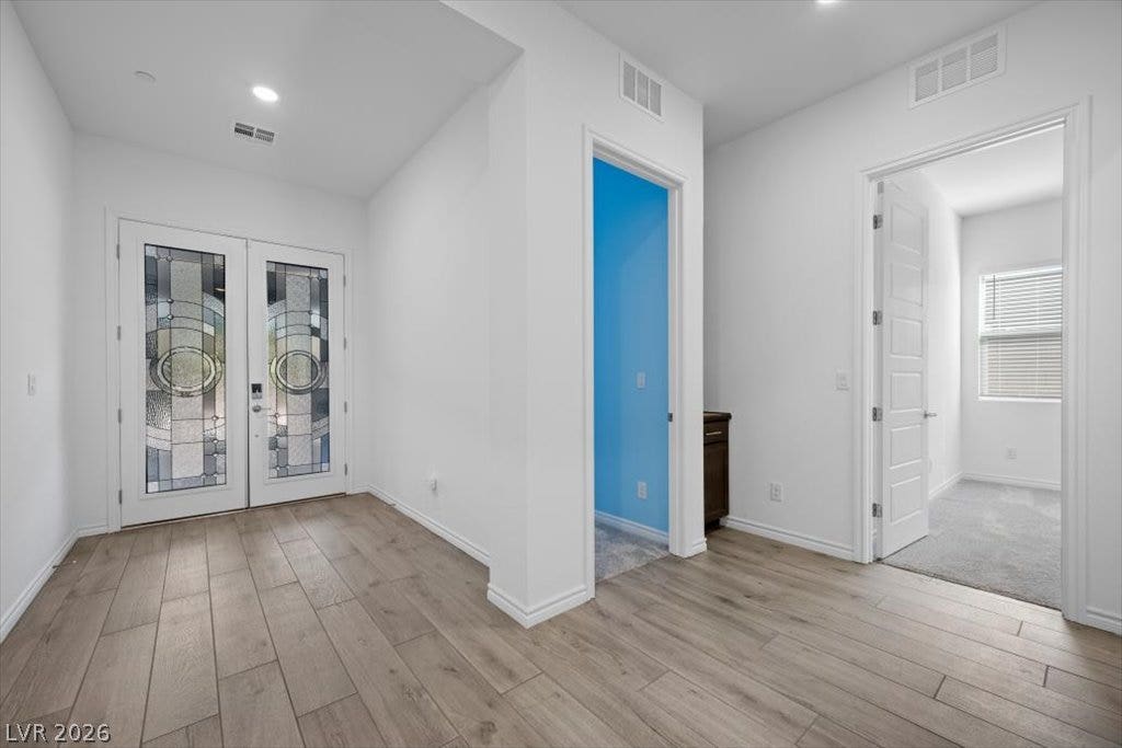 Double entry doors with decorative glass panels open to a bright, wood-look tiled foyer.