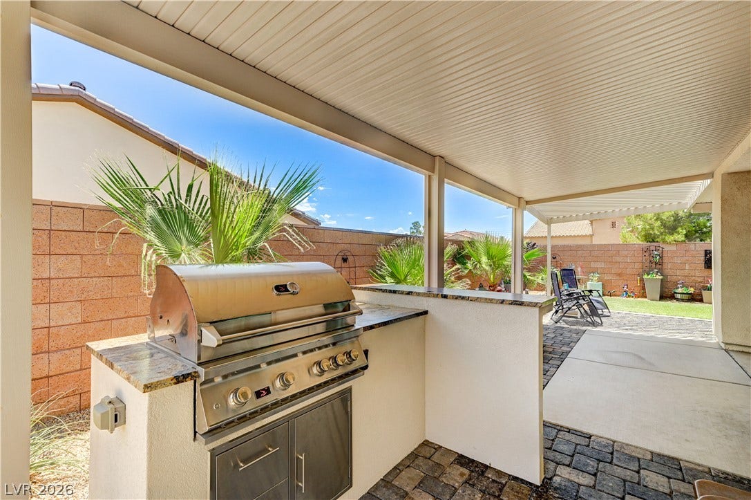 3605 Greenbriar Bluff Avenue, North Las Vegas, NV 89081 An outdoor kitchen is sheltered by a covered patio with paved flooring and stone countertops.