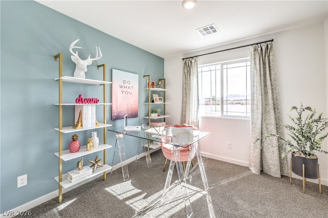 Natural light pours through a wide window illuminating the carpeted workspace.