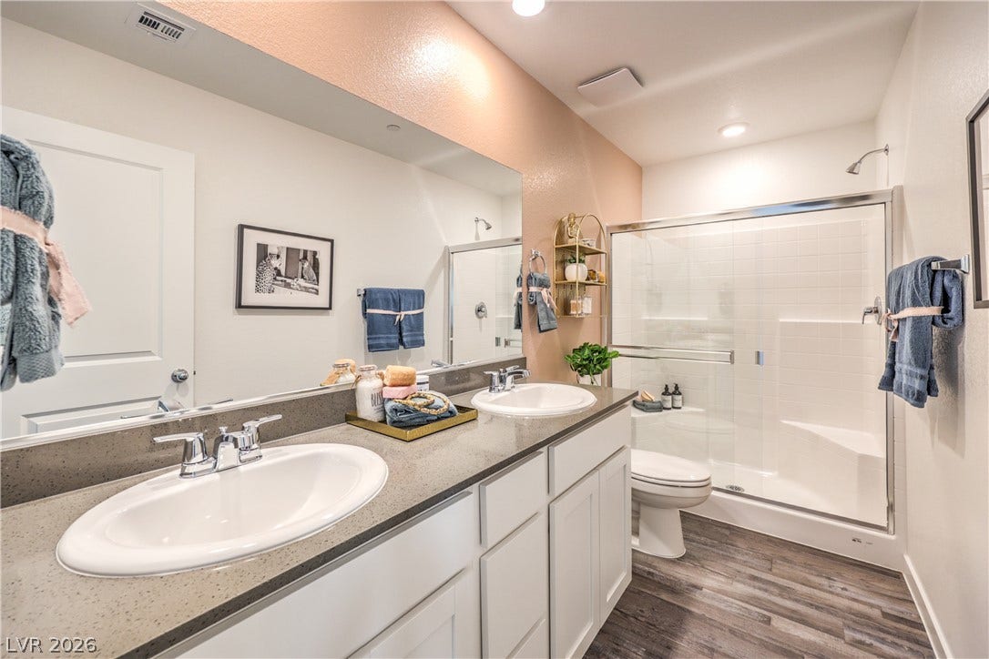 An elegant double vanity pairs with wood-look flooring and a glass-enclosed shower.