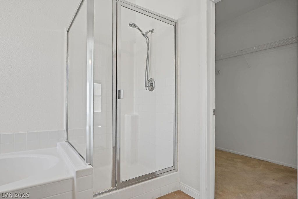 754 Solitude Point Avenue, Henderson, NV 89012 A glass-enclosed shower and adjacent soaking tub sit next to a walk-in closet entryway.