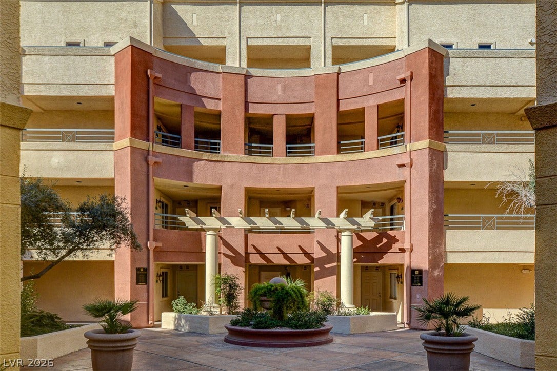 An elegant multi-level courtyard features a central stone planter under a classic pergola structure.