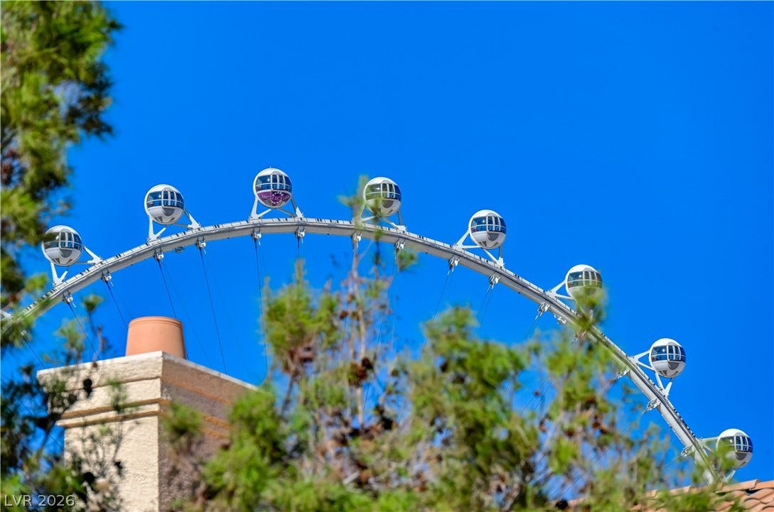 Clear blue skies and neighborhood trees frame the nearby observation wheel rising above the roofline.