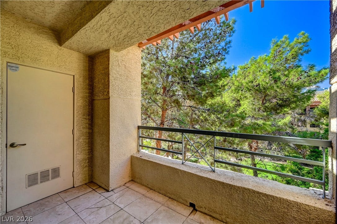 Tiled balcony offers private outdoor space overlooking mature green trees.