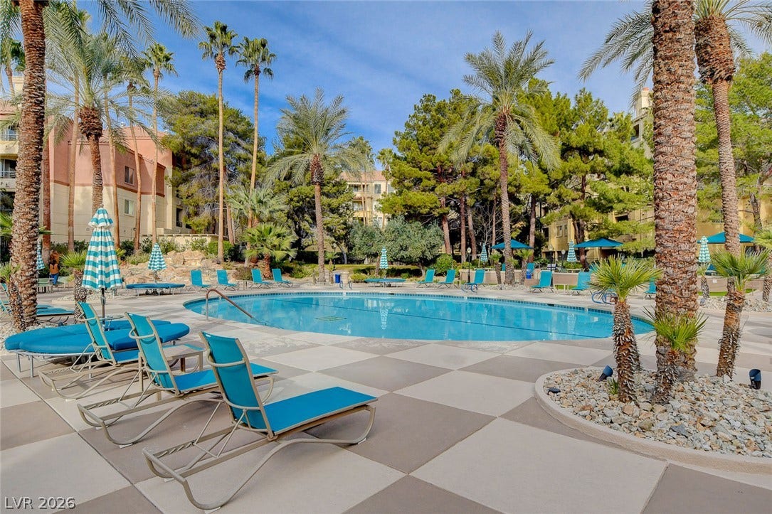 Lush palm trees surround a sparkling blue swimming pool lined with spacious tiled decking.