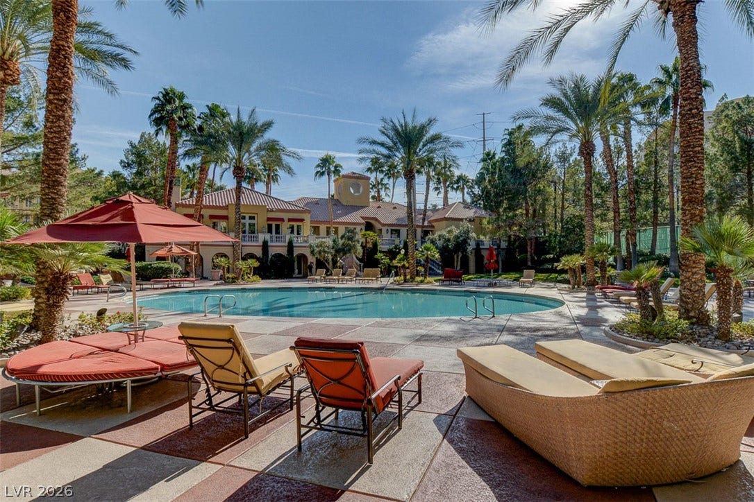 Towering palm trees surround a sprawling resort-style swimming pool lined with patterned decking.