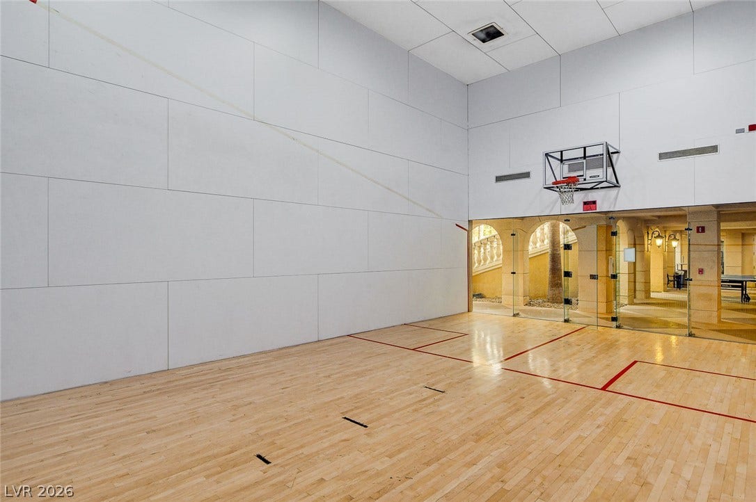 An indoor sports court boasts polished hardwood flooring and tall, paneled white walls.