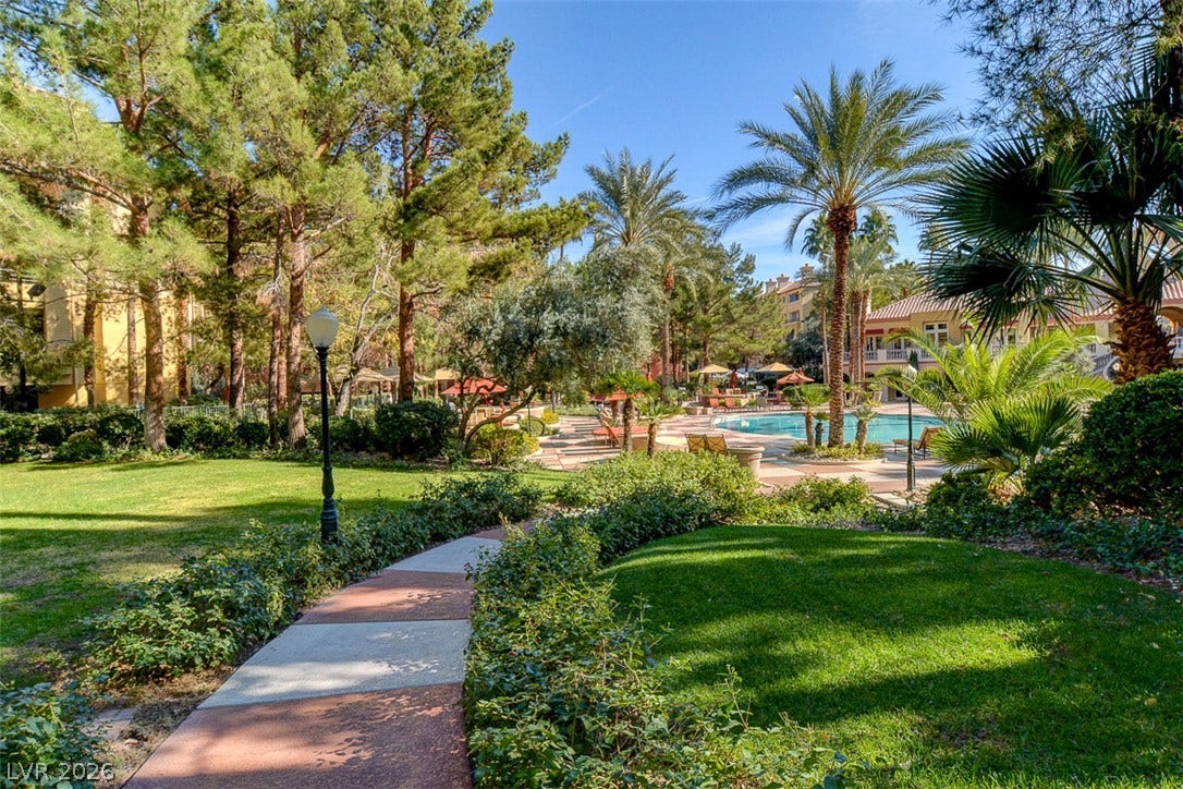 A paved path winds through manicured grounds leading toward a sparkling community pool.