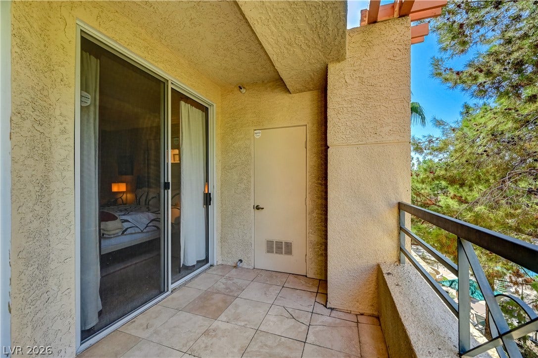 Tiled private balcony with sliding glass door entry overlooks mature trees.
