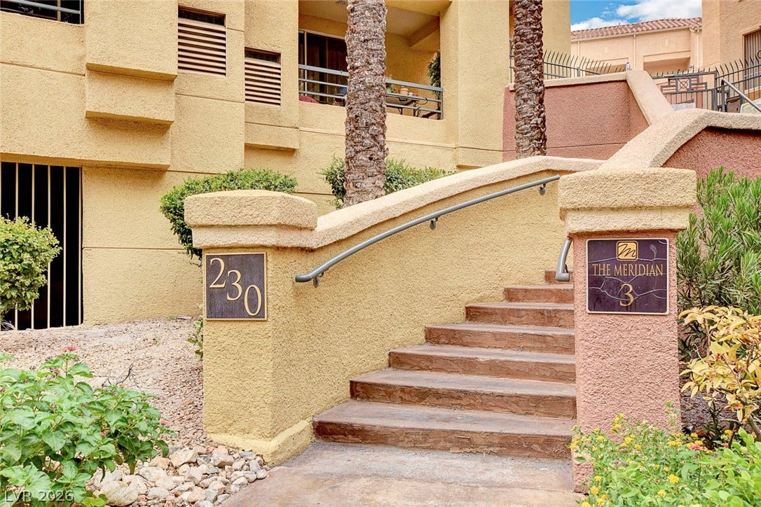 Stucco walls and concrete steps with metal handrails lead toward the upper level entryway.