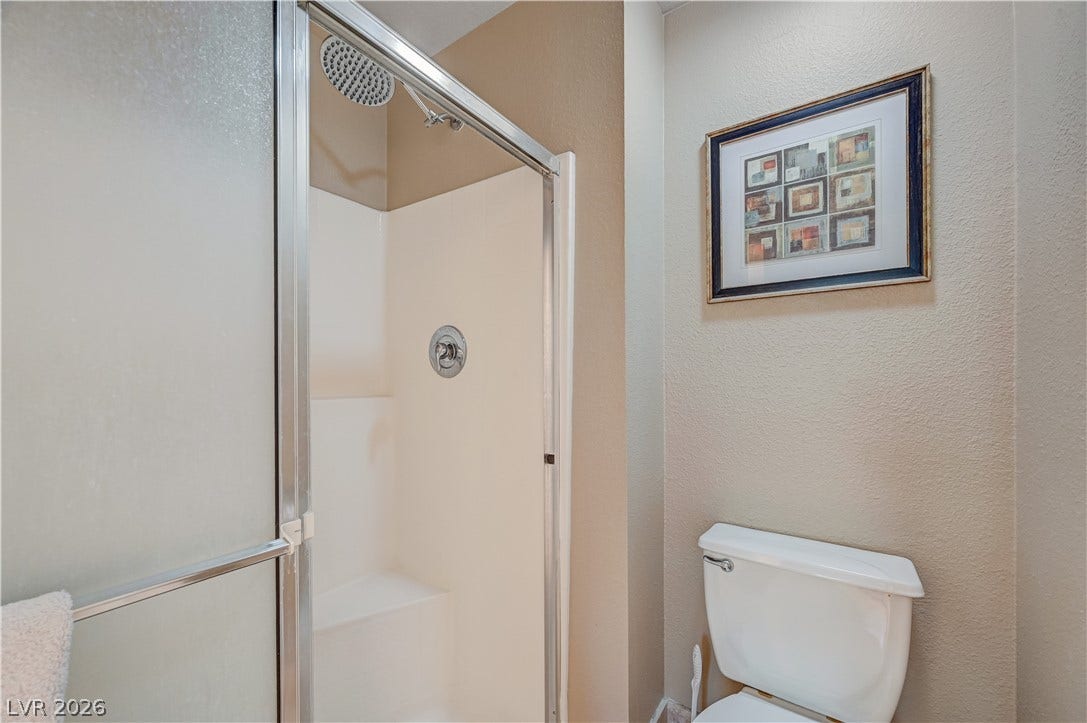 A glass-enclosed shower stall with a built-in bench sits adjacent to the toilet alcove.