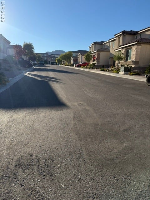 10764 Canary Blossom Avenue, Las Vegas, NV 89129 A paved suburban street guides the eye past residential facades toward distant mountain views.