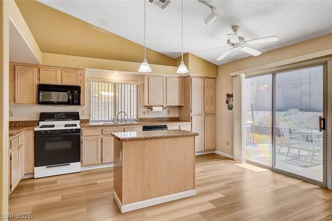 811 Rio Poco Court, Henderson, NV 89015 A spacious kitchen features wood cabinetry, a central island, and sliding glass doors opening outside.