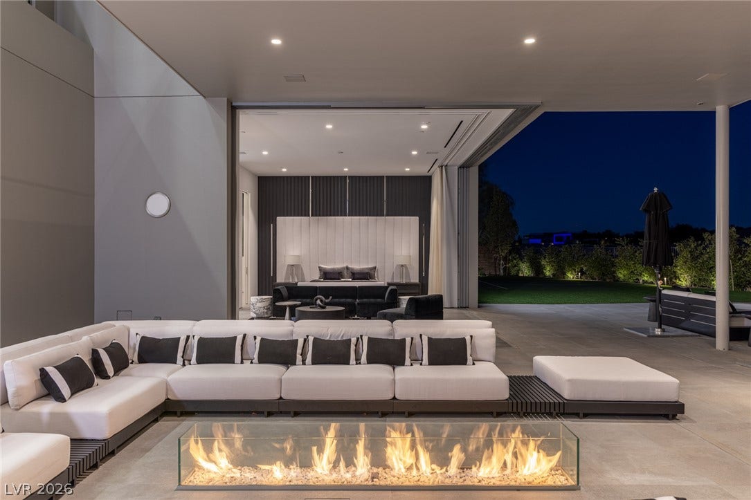 An inviting outdoor lounge with a sleek fire pit overlooks a tranquil lawn and luxurious interior.