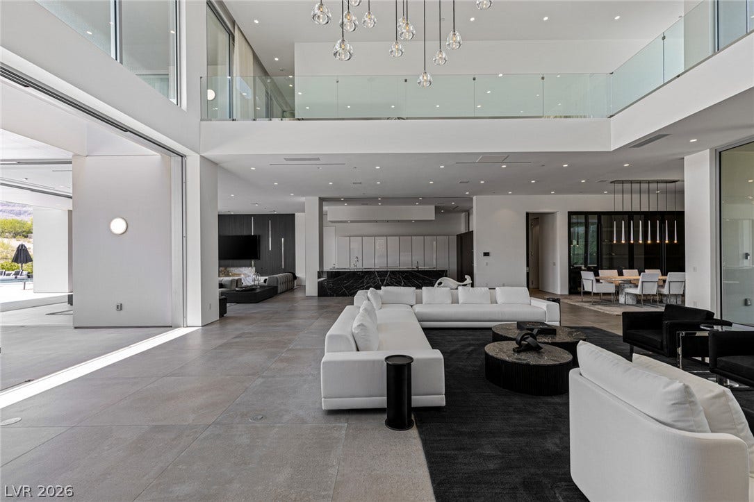 An open floorplan features soaring ceilings, a striking chandelier, and sleek tile flooring.