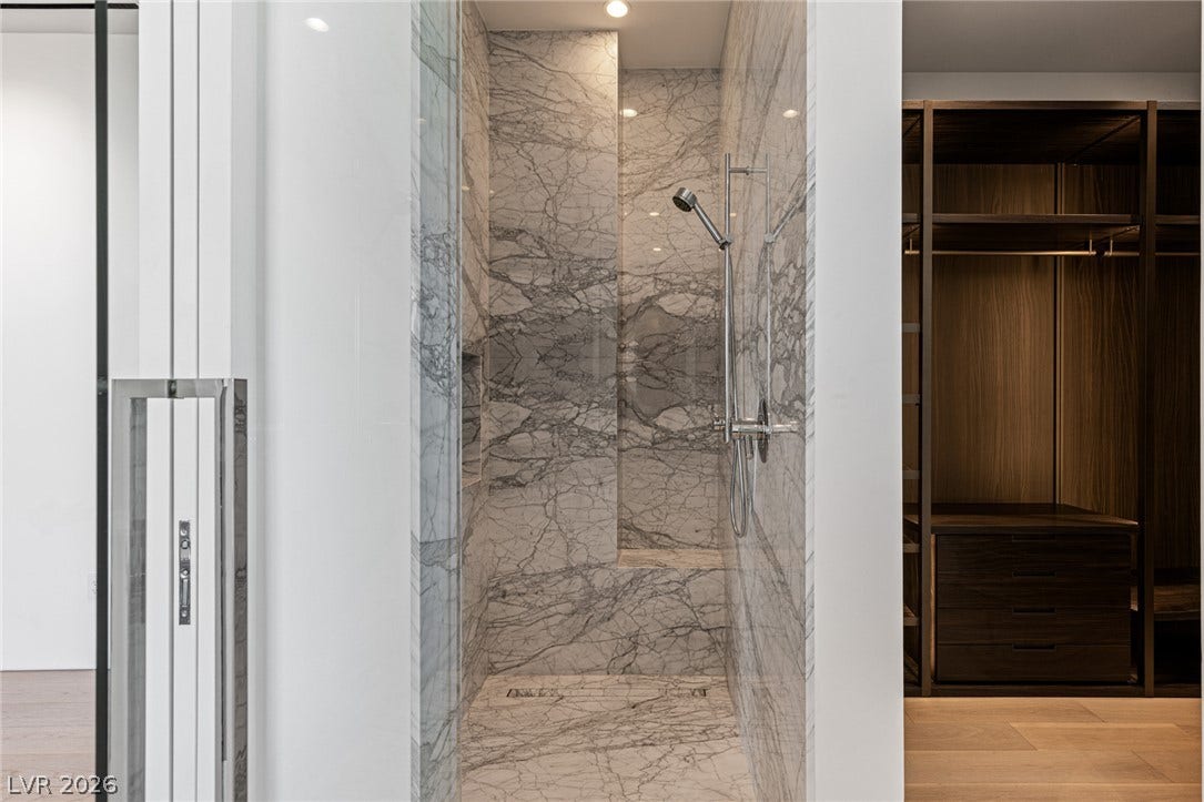 Marble-clad shower offers a serene bathing experience adjacent to a well-organized walk-in closet.