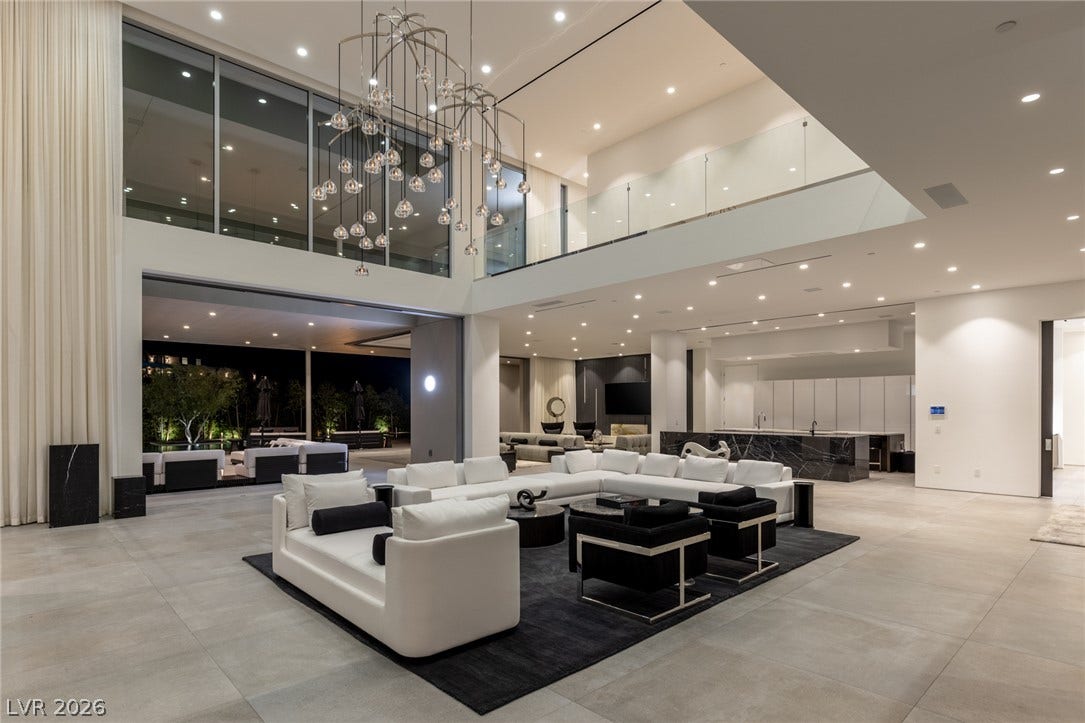A grand living space with towering windows and a modern chandelier flows into an outdoor entertainment area.