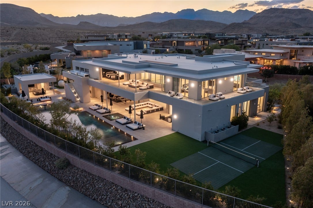 An impressive modern dwelling boasts a shimmering pool and private tennis court against a rugged mountain backdrop.
