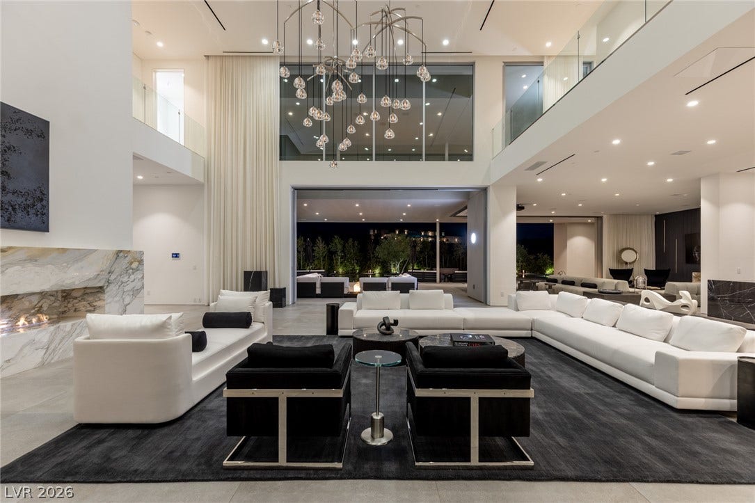 A grand, double-height living room featuring an artistic chandelier and a wall of glass overlooking a private exterior space.
