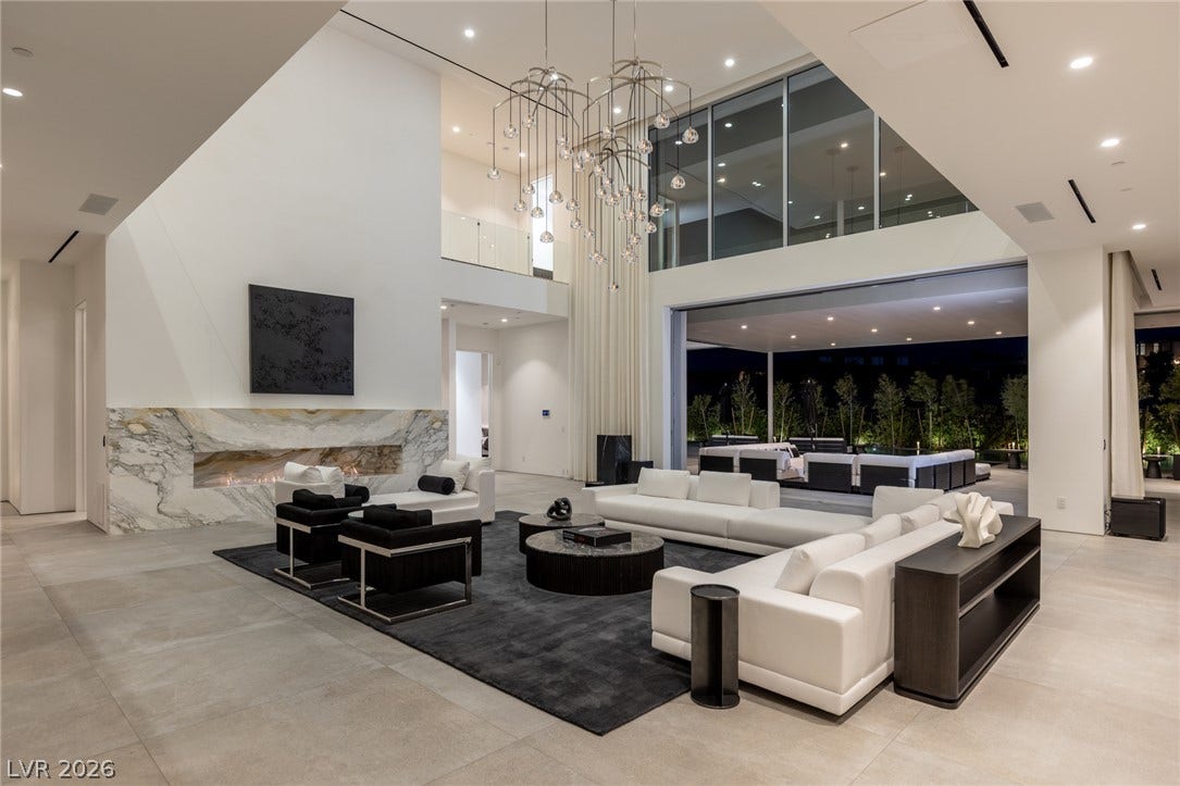 An open-concept living area features a grand fireplace and sliding glass doors revealing an outdoor living space.
