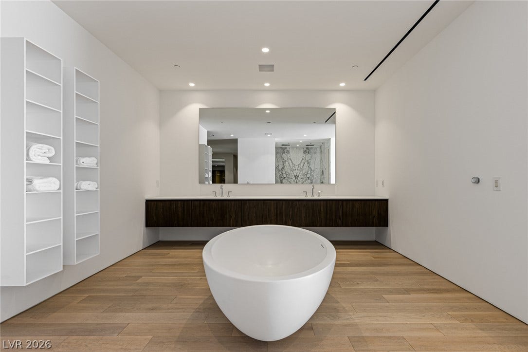 A deep soaking tub anchors this bathroom with a floating dual vanity and sleek wood flooring.
