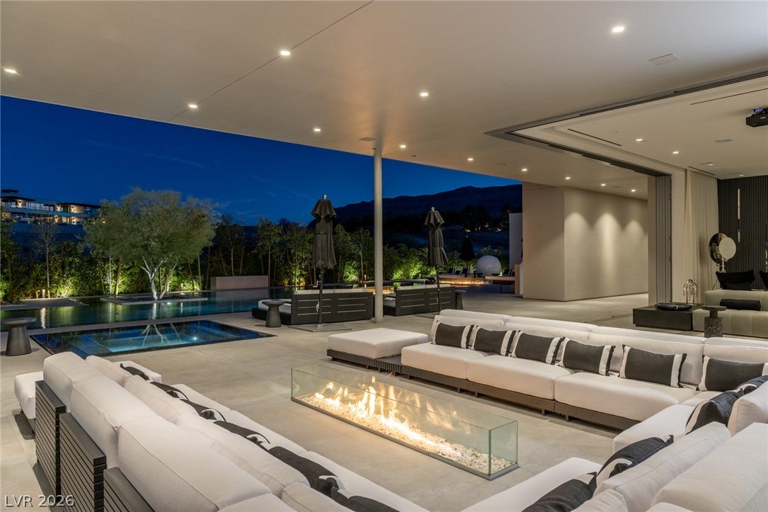 An inviting outdoor living area features a linear fire pit, comfortable seating, and a shimmering pool under the evening sky.