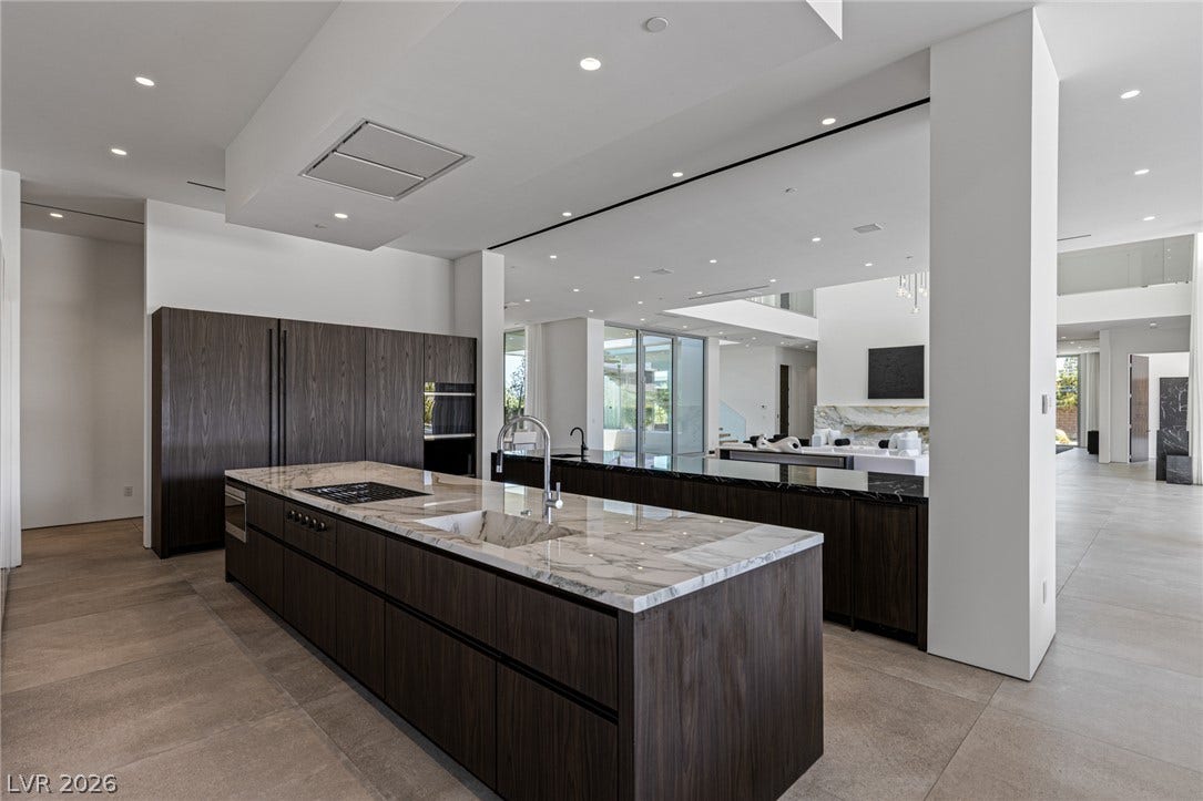 An open-concept kitchen features a large marble-topped island with integrated appliances, flowing into a spacious living area.