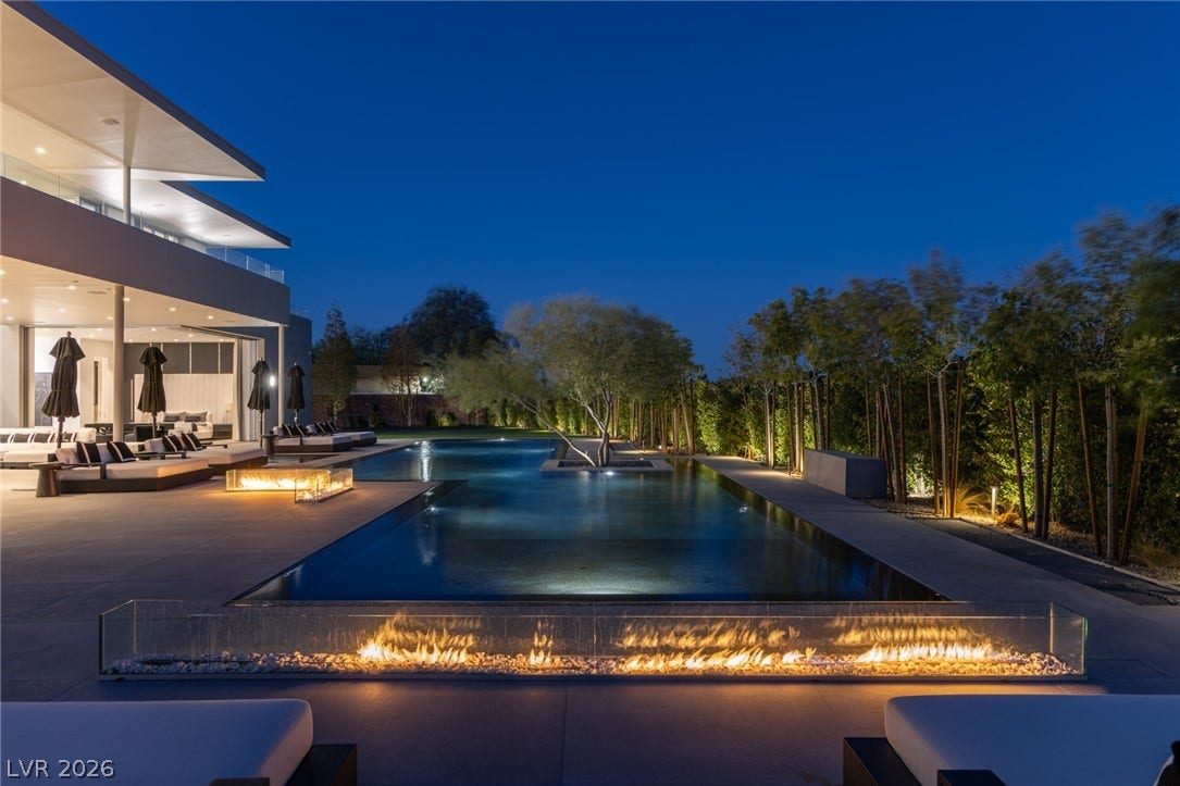 An illuminated backyard oasis featuring a chic pool with a captivating fire feature.