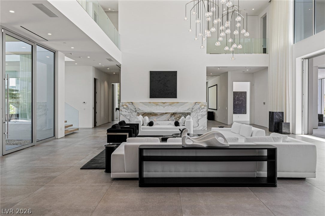 A grand, contemporary living space features soaring ceilings and a sleek fireplace with a marble surround.